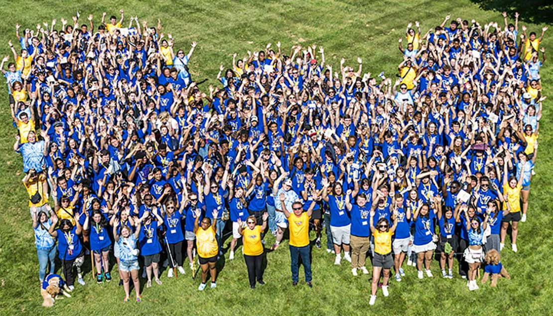 Webster students, chancellor, president stand in shape of W on the Univesity lawn.