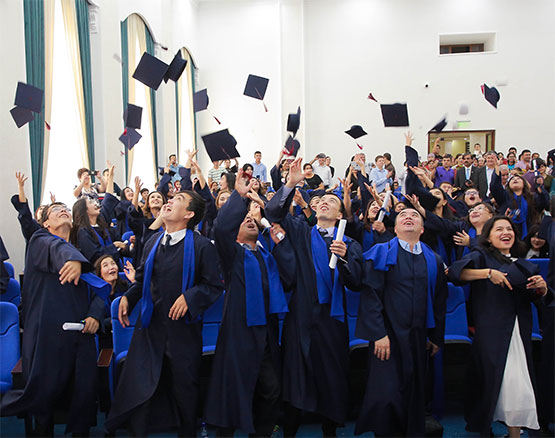 A group of Tashkent graduates throwing their hats in the air and smiling.