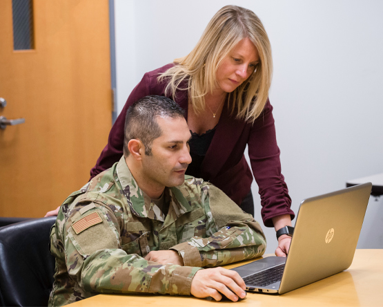 A teacher assists a military student on a laptop.